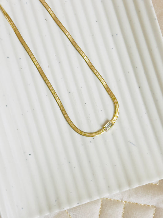 Gold snake chain necklace on a textured white surface