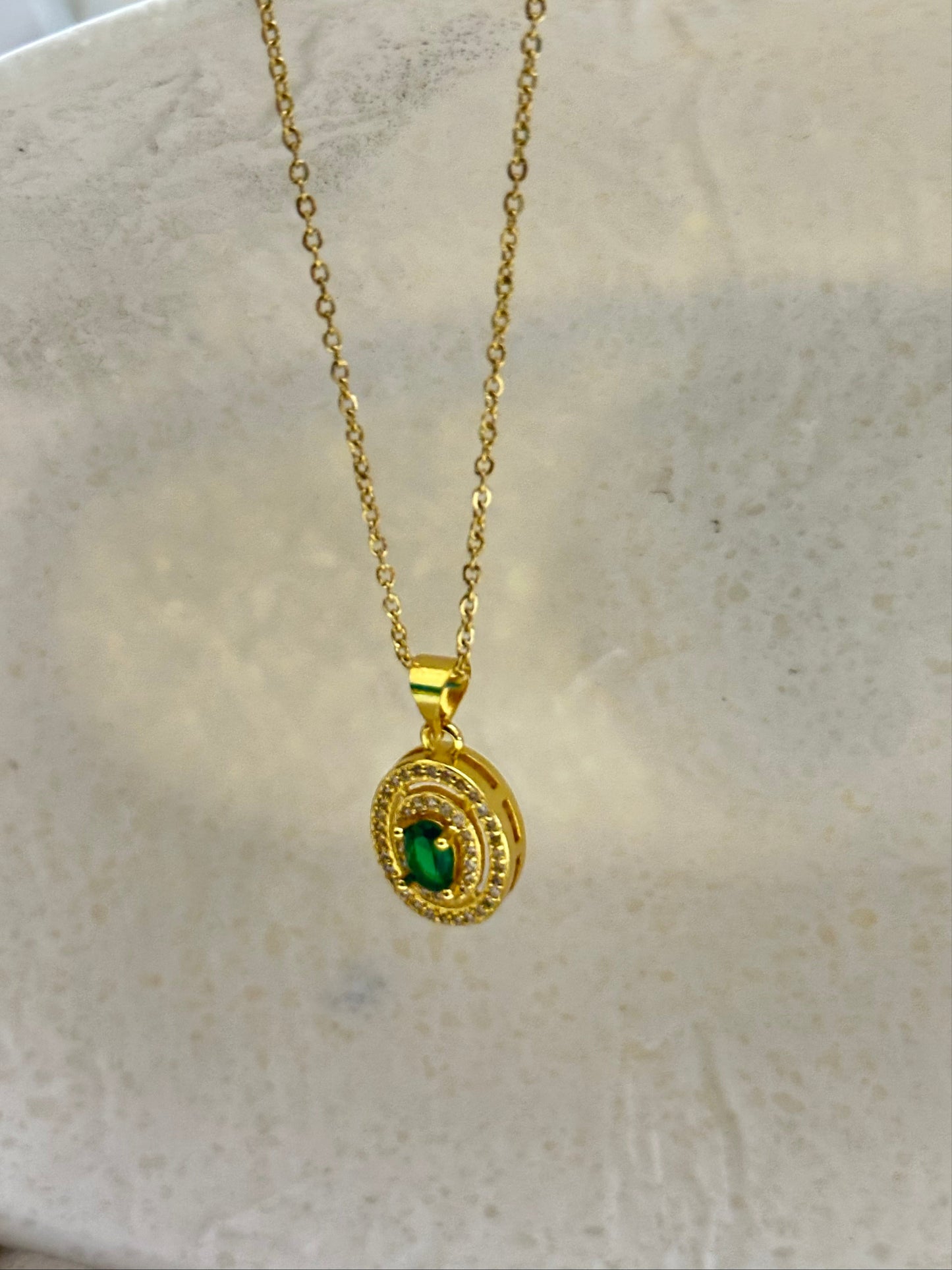 Gold necklace with a green gemstone pendant on a marble surface