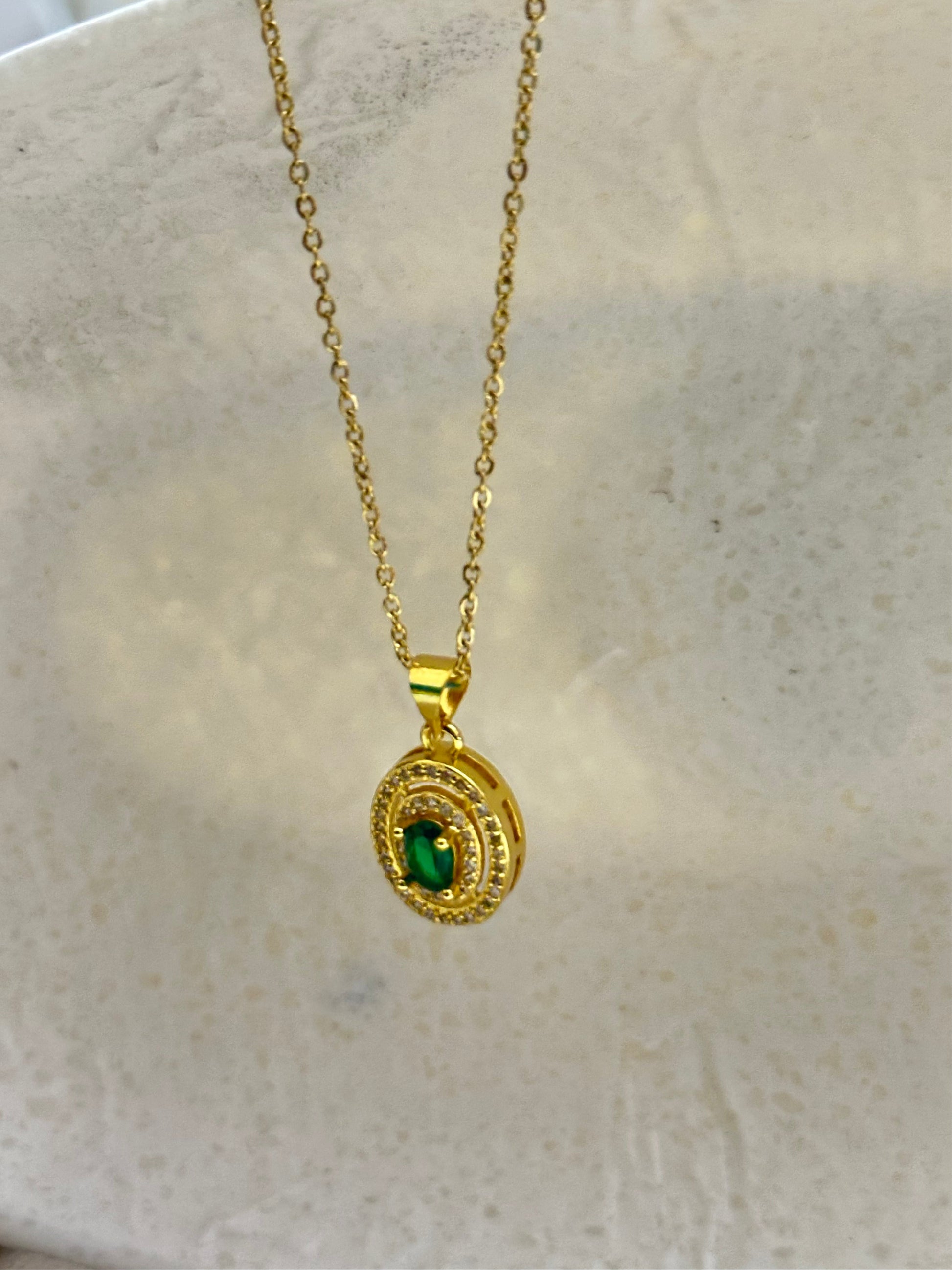 Gold necklace with a green gemstone pendant on a marble surface