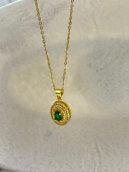 Gold necklace with a green gemstone pendant on a marble surface